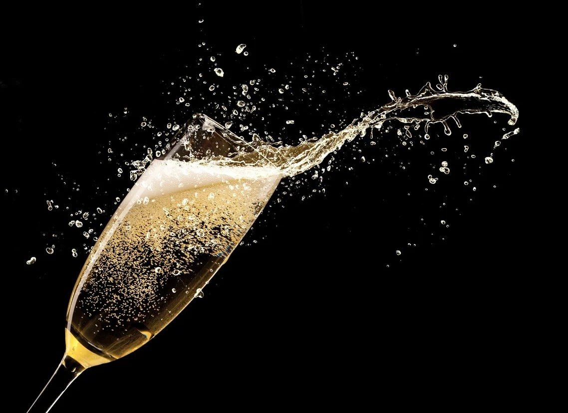 Champagne flute with golden sparkling liquid splashing out dramatically with bubbles and droplets against black background.