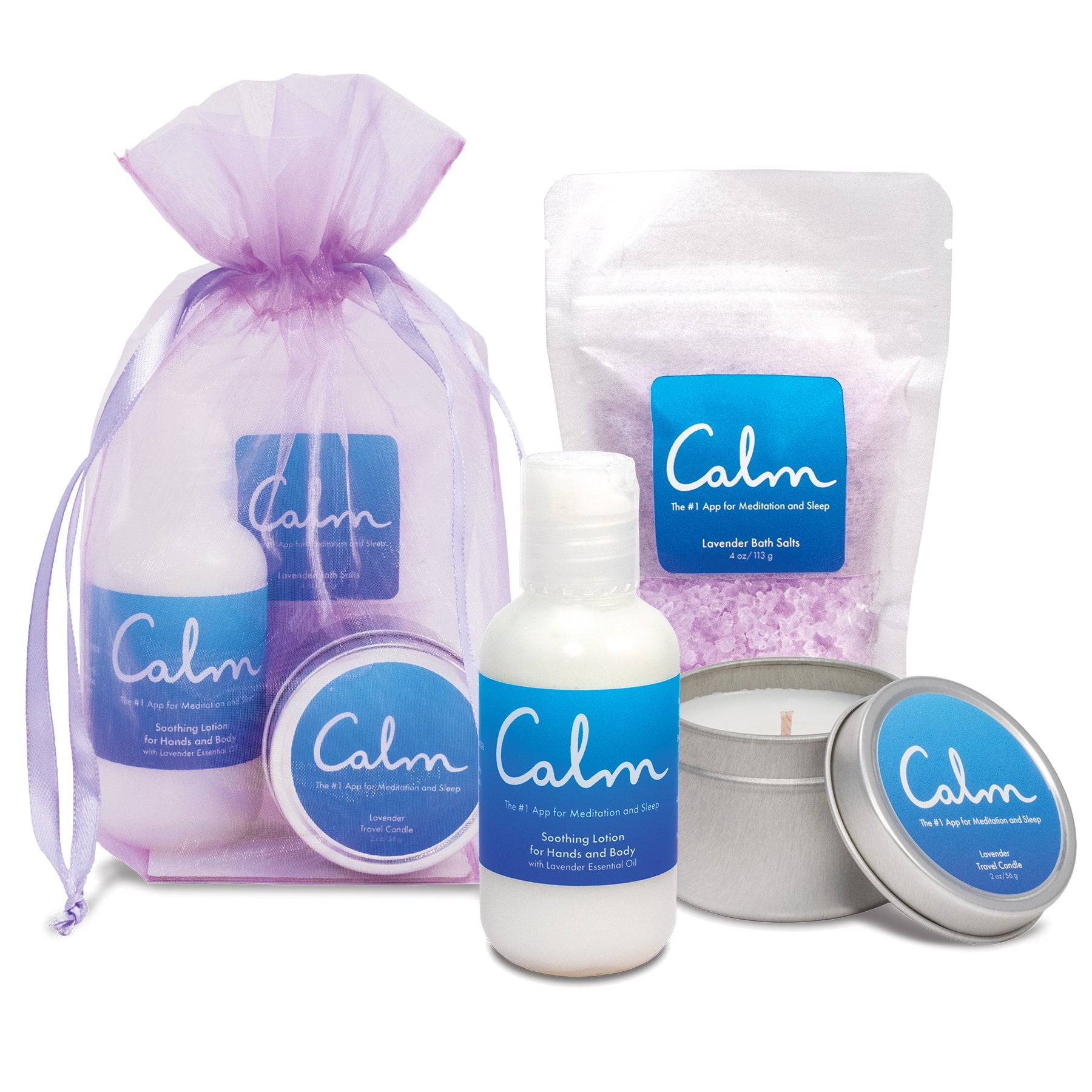 Branded spa gift set featuring lavender products with blue labels. Set includes a purple organza drawstring bag containing items, a white resealable pouch of purple lavender bath salts, a white pump bottle of soothing lotion, and a silver tin travel candle with lid. All products feature the branding and are lavender-scented spa items.