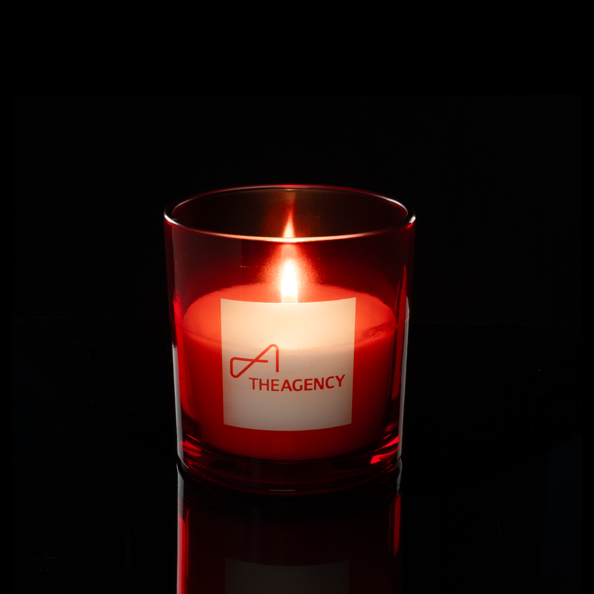 9 oz. Red glass candle with custom engraved logo from Bath Promotions, shown lit — Lit version