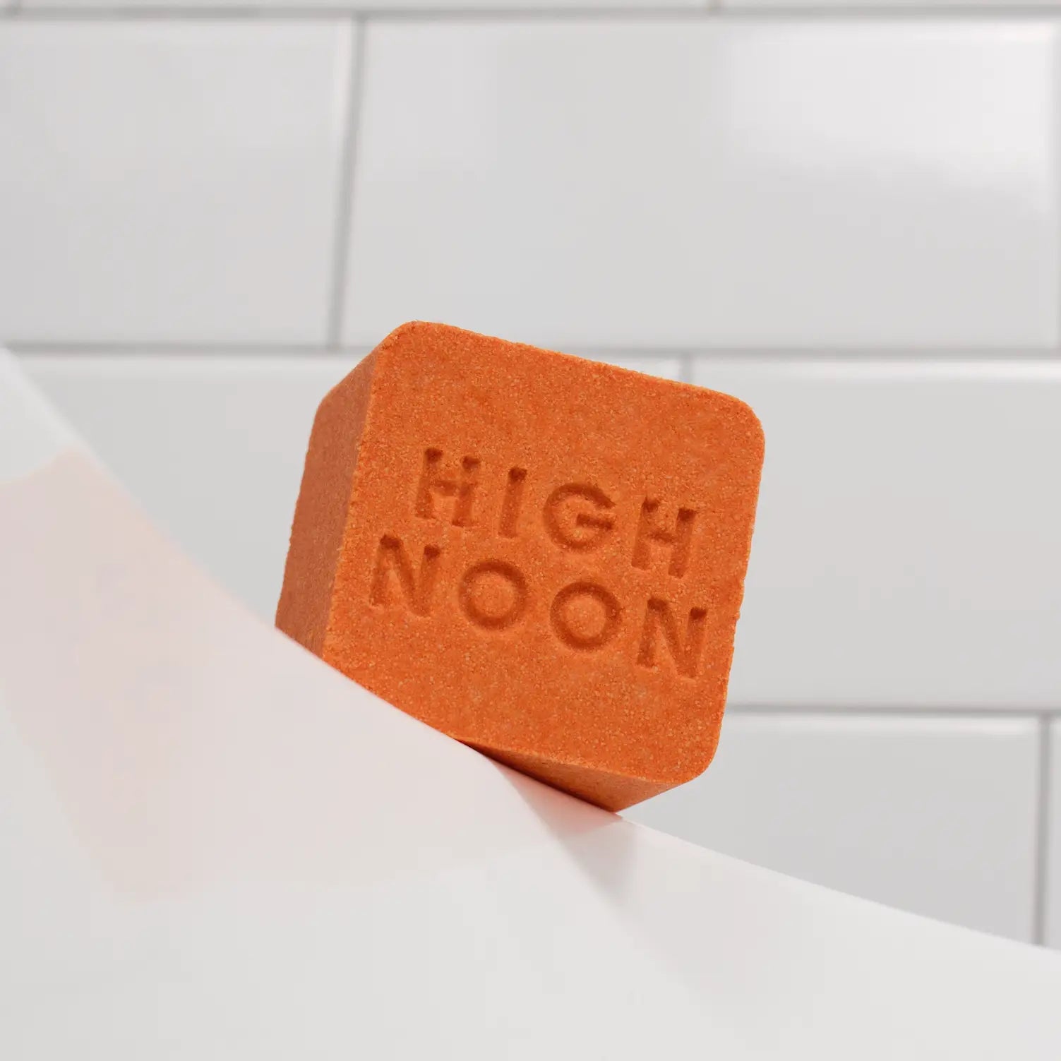 Custom-embossed artisan bath bomb in deep terracotta orange, featuring a bold debossed brand logo pressed into the surface, photographed against clean white subway tile — a bespoke branded wellness gift made in Los Angeles.