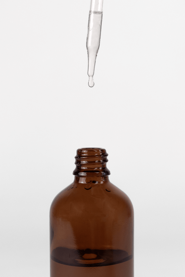 Glass dropper filled with fragrance oil filling a amber glass bottle on a white background