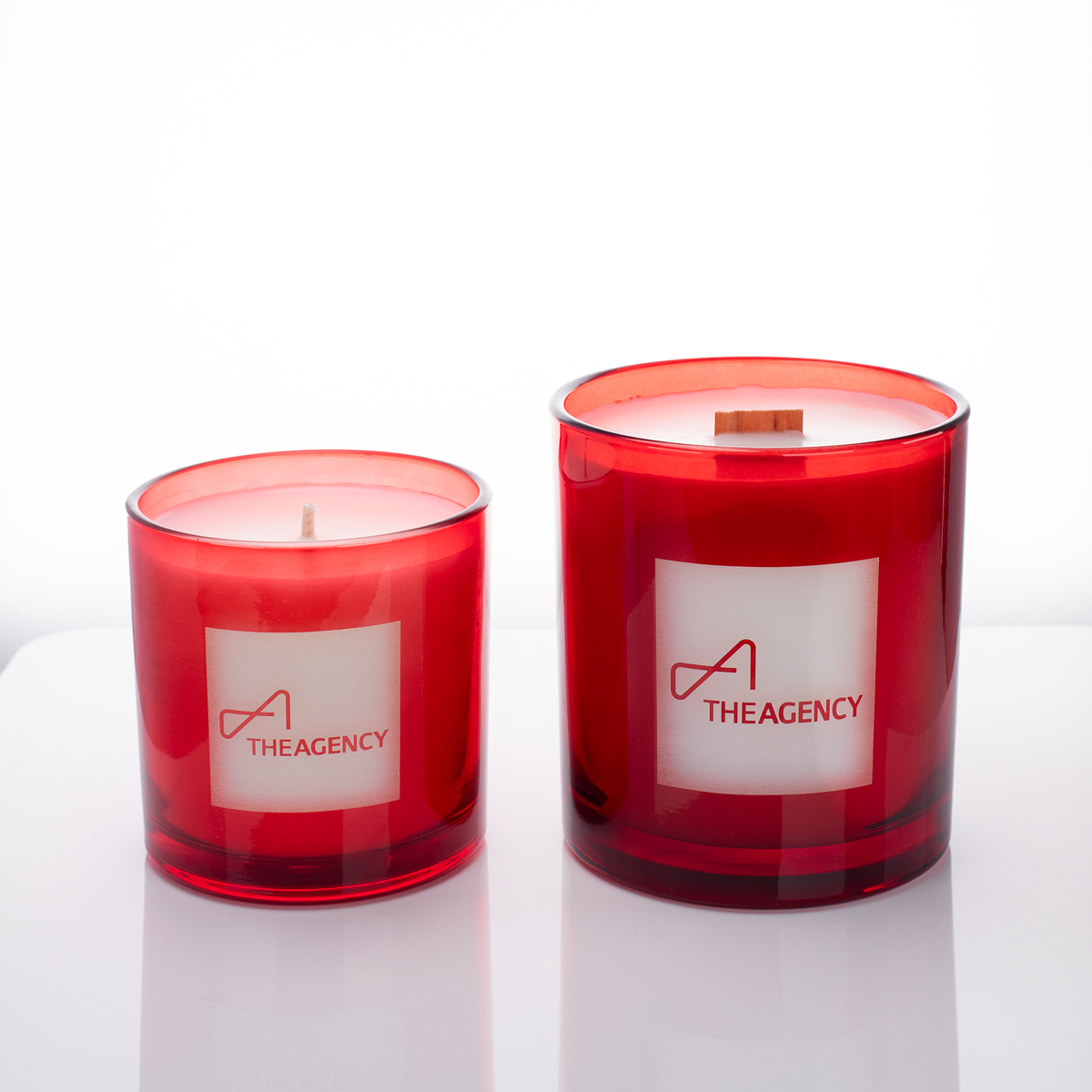 Red glass candles, 9 oz. beside 14 oz., both laser engraved with the same logo, from Bath Promotions