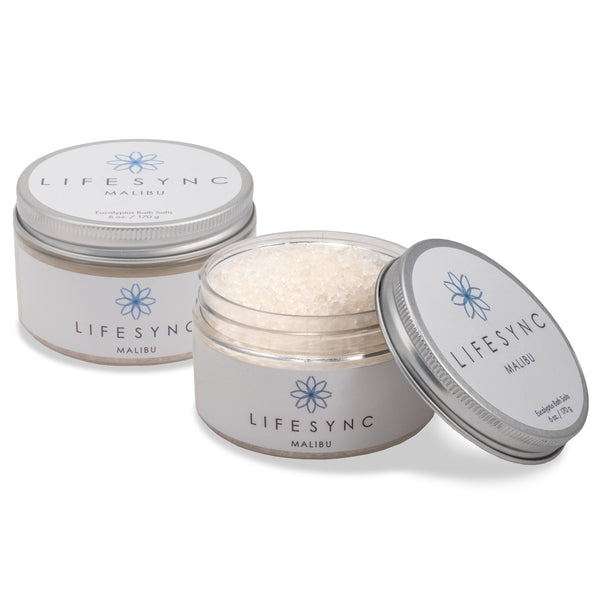Two 6 oz clear jars with silver screw-on lids and white labels. One jar is closed, the other is open revealing white bath salts inside.