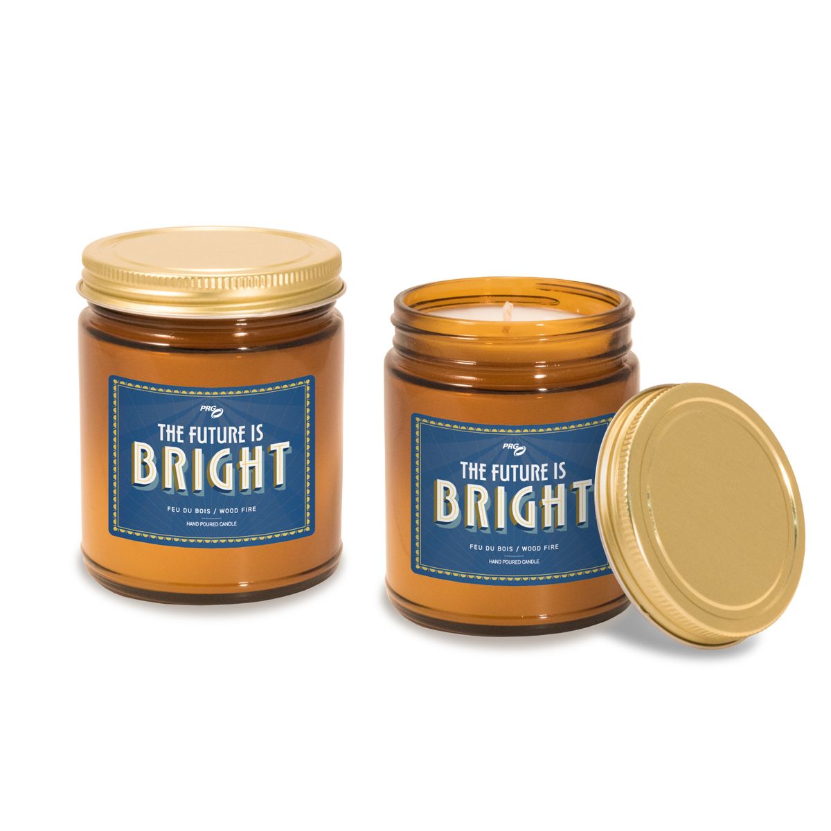 Two 8 oz amber glass apothecary jar candles with gold screw-on lids and navy blue labels. One jar is closed with lid on top, the other is open showing the lit candle inside with the lid placed beside it