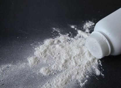White baby powder spilled from an overturned white plastic bottle onto a dark gray surface.