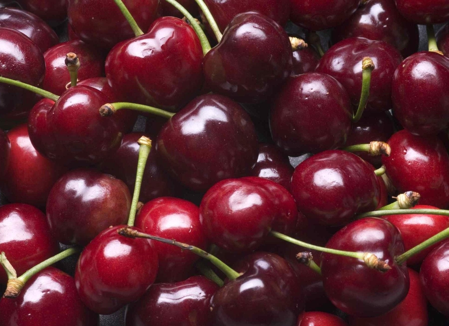 Fresh red cherries with green stems clustered together, showing their glossy, deep red skin and natural shine.