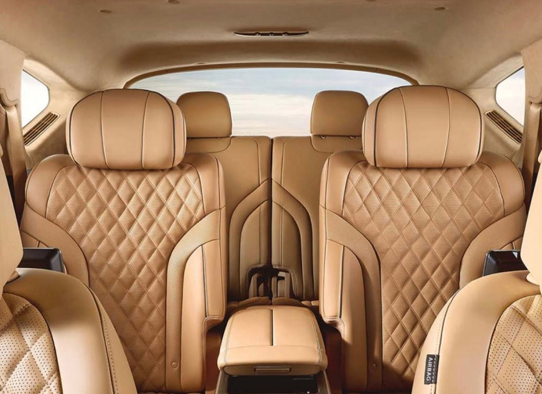 Luxury car interior with tan quilted leather seats featuring diamond-pattern stitching, showing front captain's chairs and rear bench seating in a spacious cabin with panoramic sunroof.
