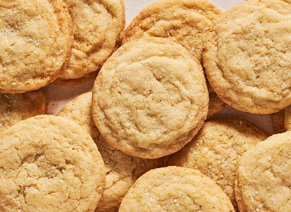 Golden brown sugar cookies with cracked surfaces and granulated sugar coating arranged on brown parchment paper.