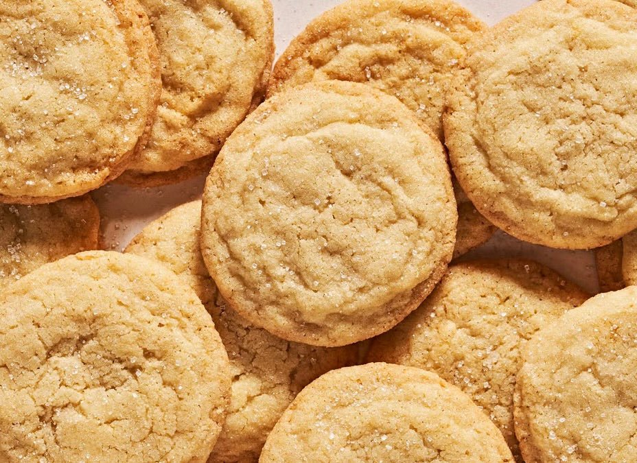 Golden brown sugar cookies with cracked surfaces and granulated sugar coating arranged on brown parchment paper.