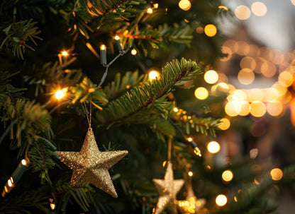 Christmas tree with green pine branches decorated with golden glittery star ornaments and warm white string lights creating soft bokeh effect in background.