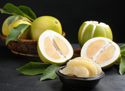 Fresh white grapefruit halves and segments with green leaves in wicker basket and black bowl on dark surface.