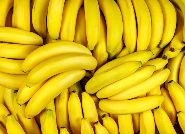 Multiple bunches of ripe yellow bananas arranged closely together, filling the entire frame.