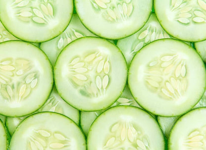 Fresh cucumber slices arranged in overlapping pattern, showing pale green flesh and white seeds.