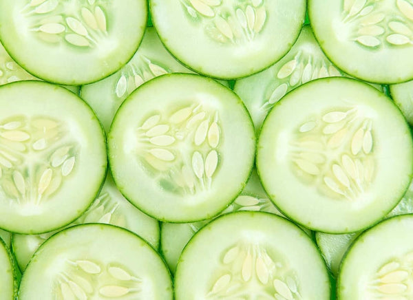 Fresh cucumber slices arranged in overlapping pattern, showing pale green flesh and white seeds.