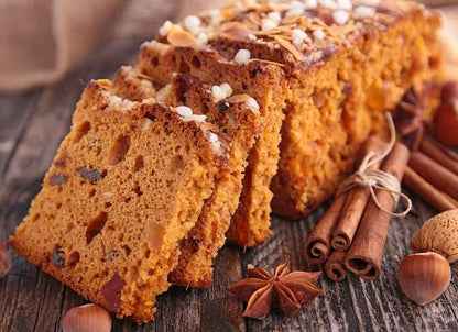 Sliced spice bread with nuts and dried fruit on wooden surface with cinnamon sticks, star anise, and hazelnuts.