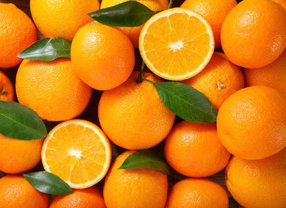 Fresh oranges with textured peels and two halved oranges showing bright flesh, scattered with green leaves.