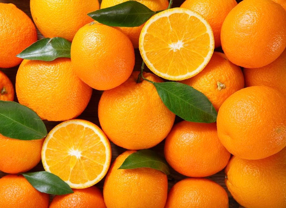 Fresh oranges with textured peels and two halved oranges showing bright flesh, scattered with green leaves.