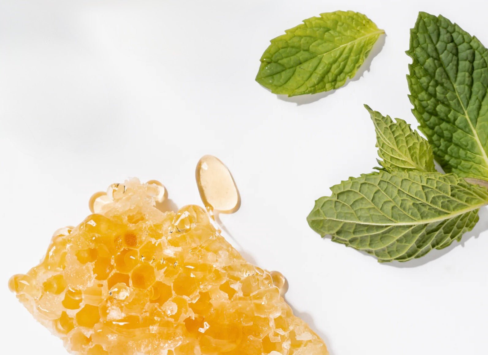 Golden honeycomb with hexagonal cells and fresh green mint leaves with textured surfaces on white background.