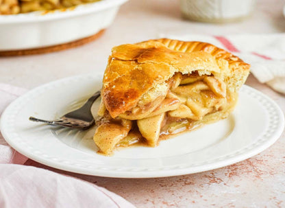 Slice of golden apple pie with flaky crust and cinnamon apple filling on white plate with fork.