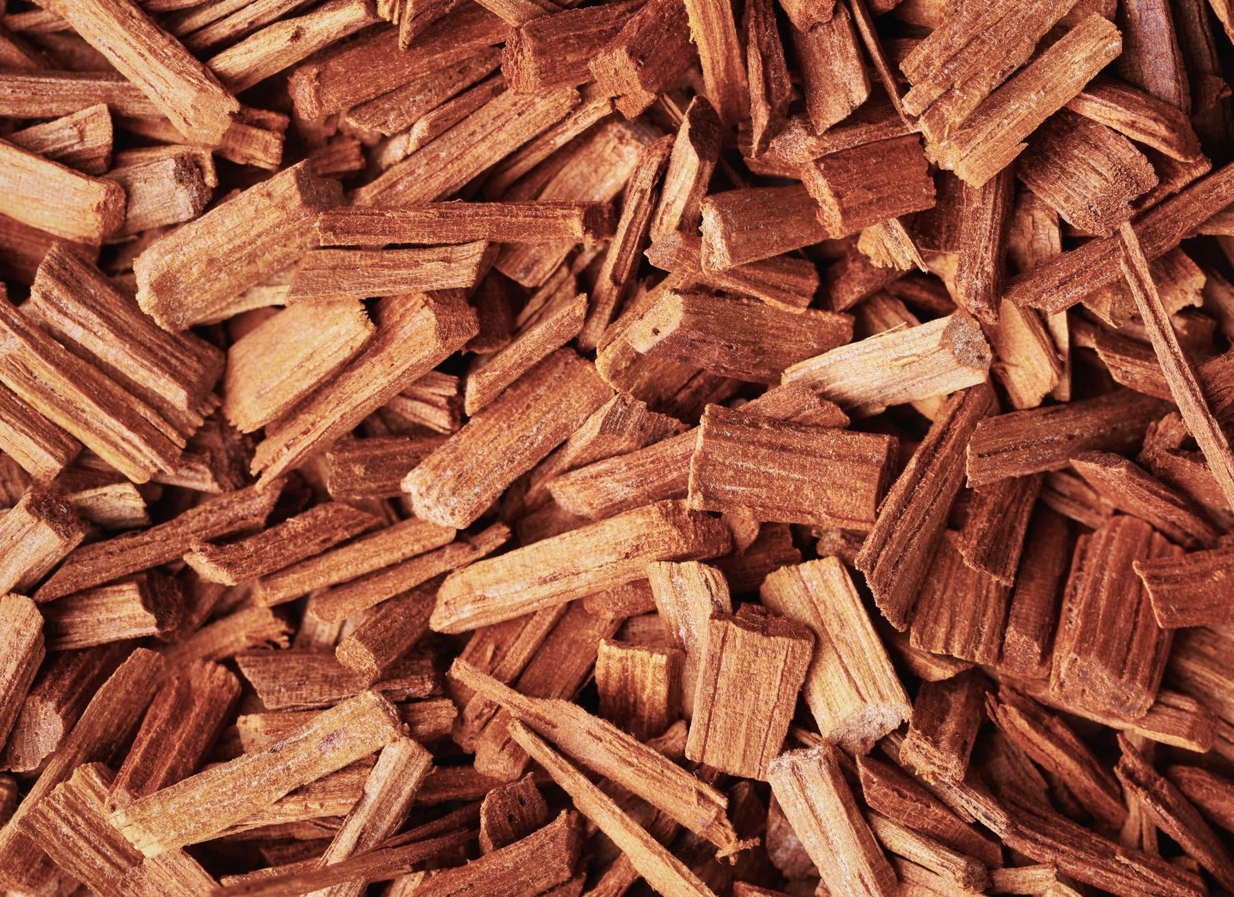 Small pieces of reddish-brown sandalwood chips scattered densely across the entire frame showing natural wood grain.
