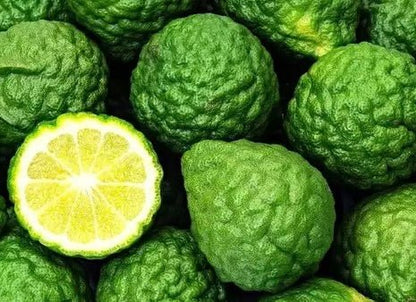 Green bergamot citrus fruits with bumpy textured skin and one halved showing bright yellow segmented flesh.