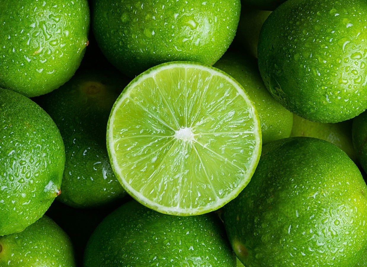 Fresh green limes with water droplets and one halved lime showing bright segmented flesh in center.