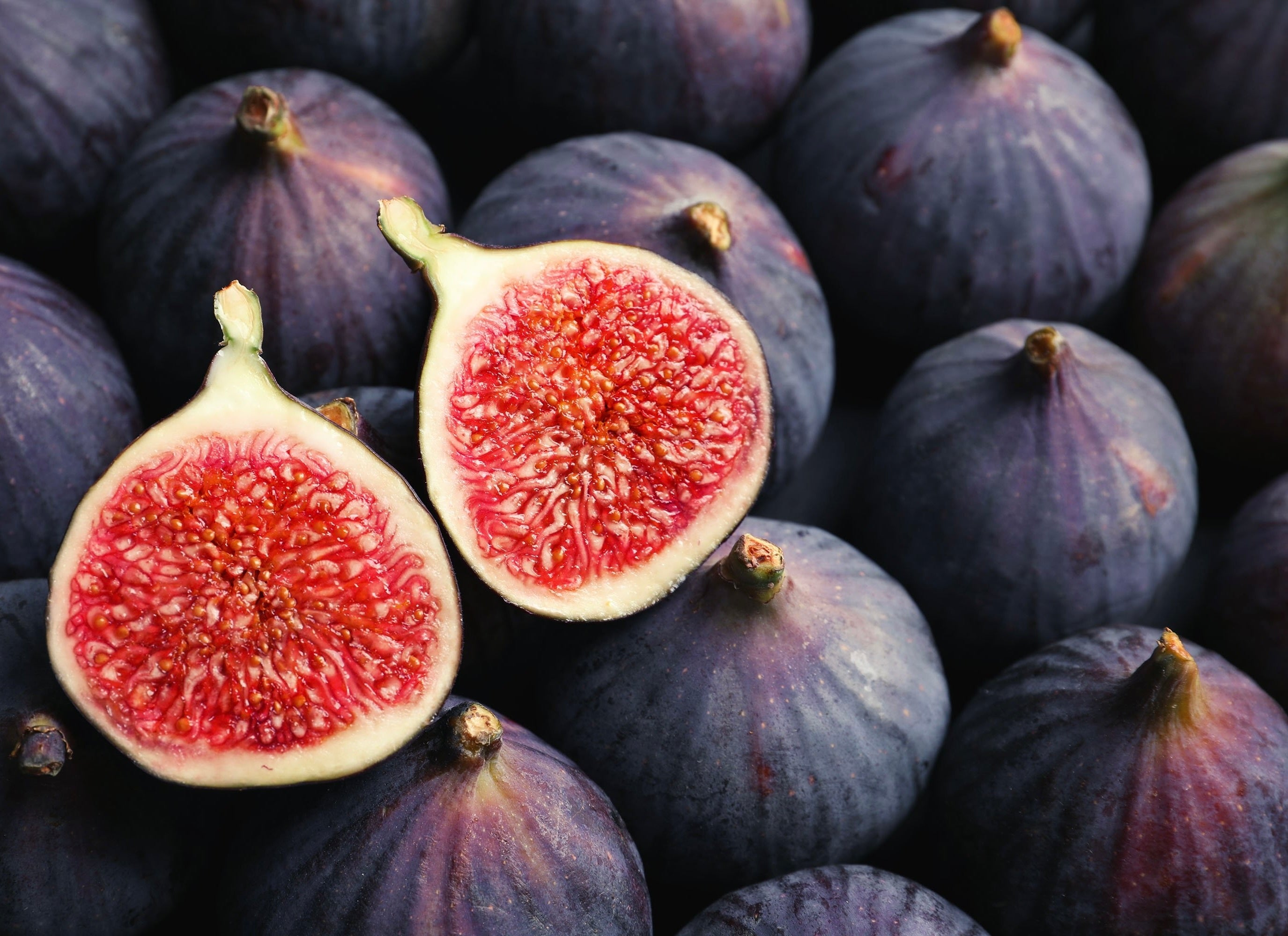 Fresh purple figs with two halved showing bright red seeded flesh surrounded by whole figs with dark skin.