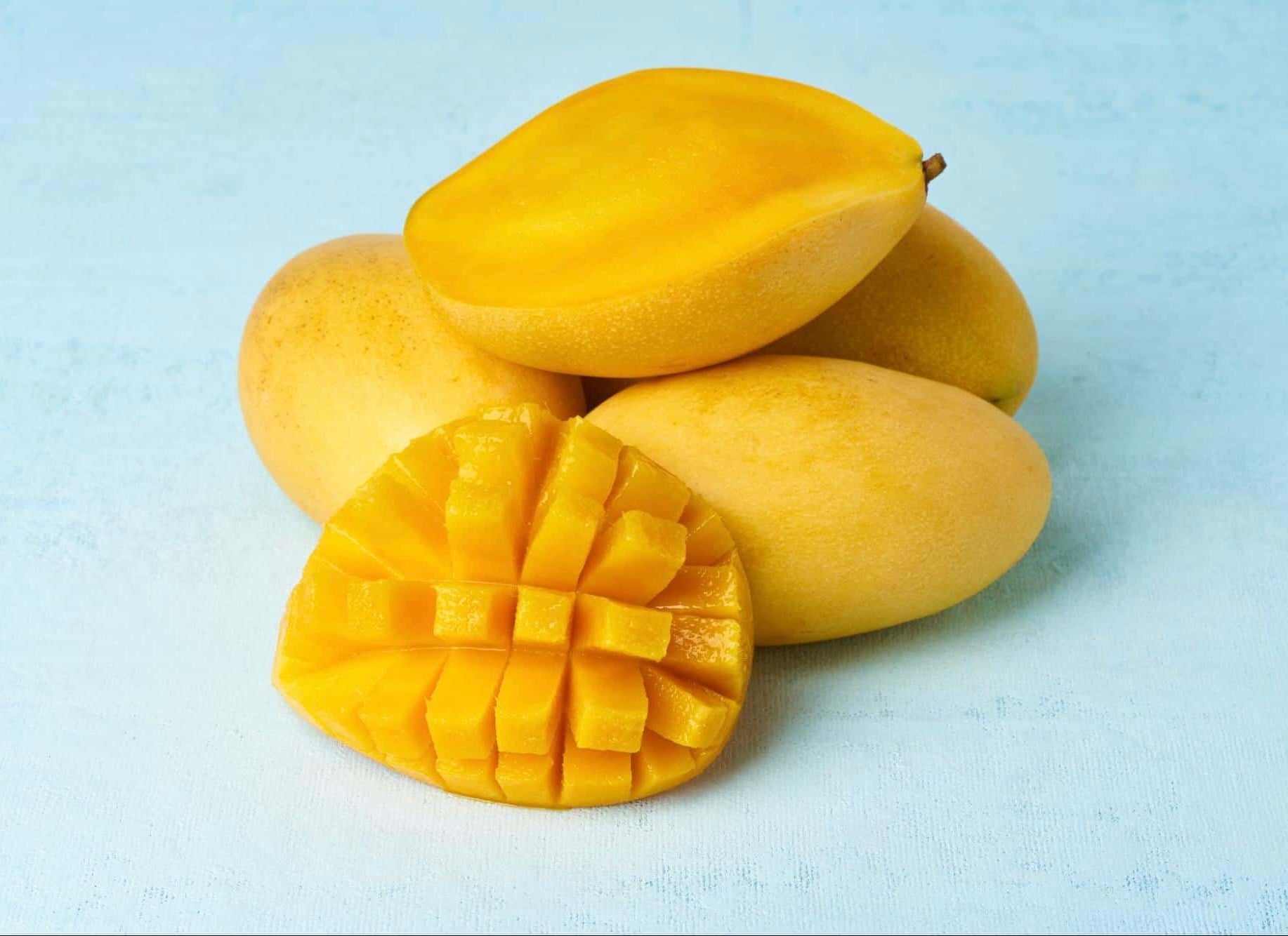 Fresh yellow mangoes with one cut showing bright orange flesh diced in crosshatch pattern on white surface.