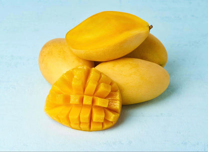 Fresh yellow mangoes with one cut showing bright orange flesh diced in crosshatch pattern on white surface.