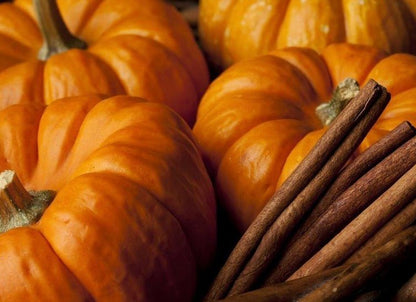 Orange pumpkins with ribbed surfaces and green stems alongside bundle of brown cinnamon sticks in close-up view.