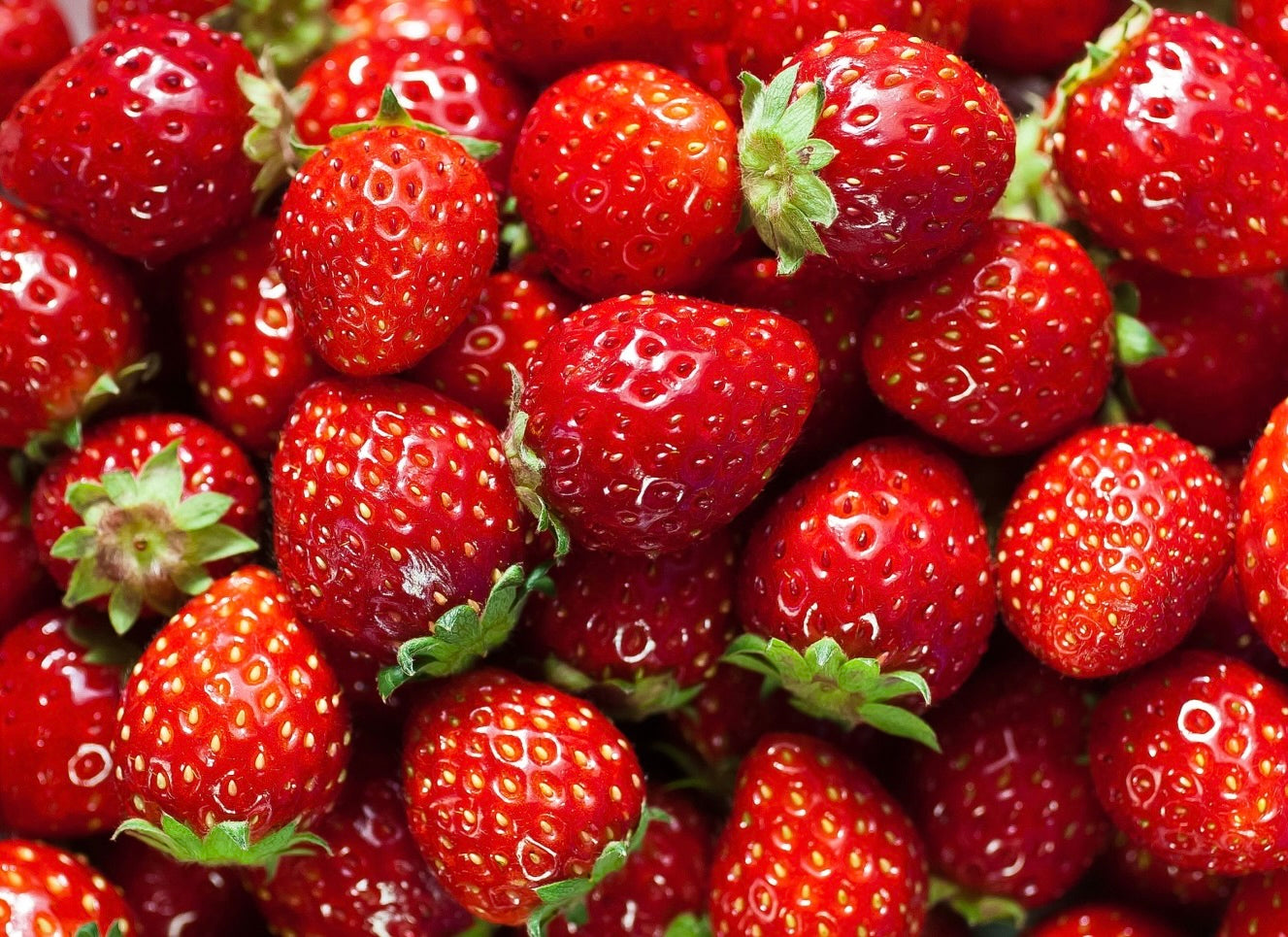 Fresh red strawberries with textured surfaces and green leafy tops arranged closely together filling the entire frame.