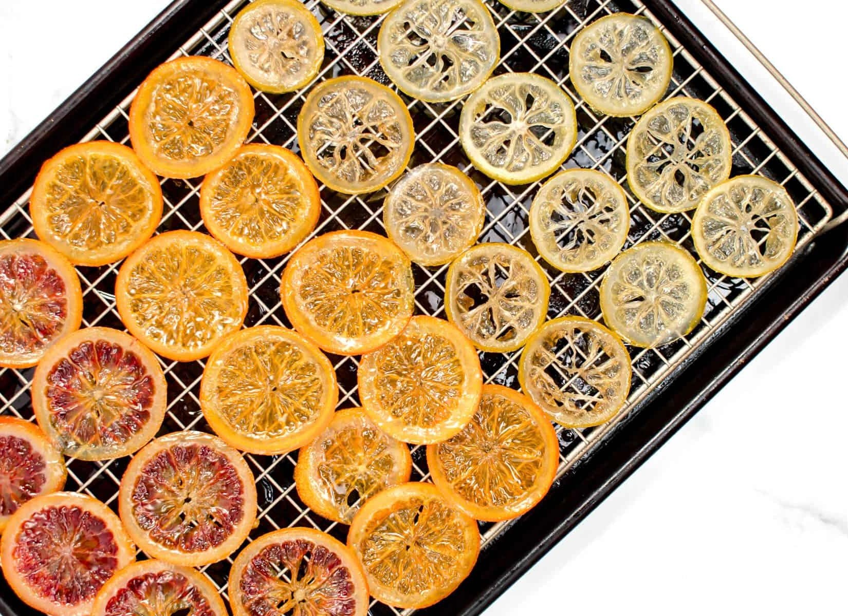 Dehydrated citrus slices in various stages of drying on black wire rack, showing orange, yellow, and red colors.