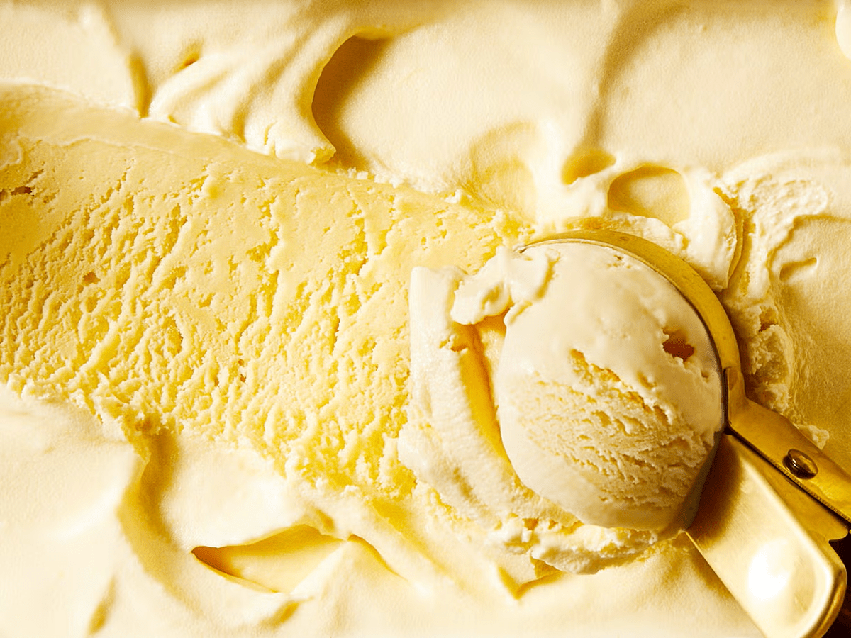 Creamy yellow vanilla ice cream with ice cream scoop creating rounded portion, showing smooth texture and swirled patterns.